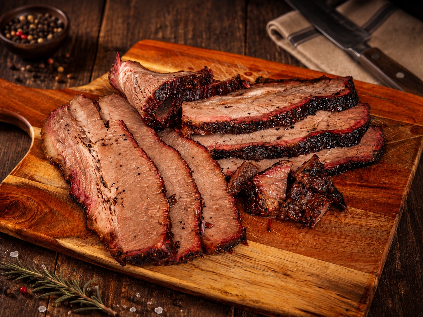 Sliced smoked brisket with a dark bark on a wooden serving board